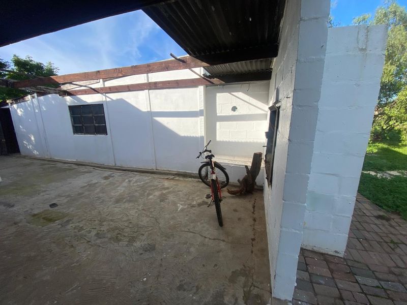 A covered outdoor patio area featuring concrete flooring, exposed timber beams, and painted cinder block walls, offering potential for an outdoor entertainment space.