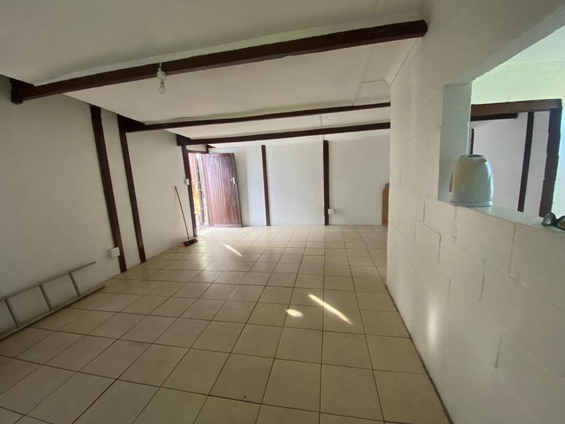 An empty living area featuring exposed timber ceiling beams, ceramic floor tiles, and a convenient pass-through window to the adjacent space.