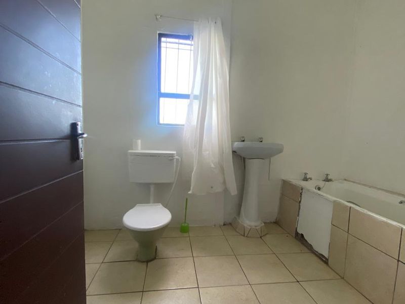 A functional bathroom featuring a pedestal basin, toilet, and bathtub with tiled flooring, requiring cosmetic updates to improve its overall condition.