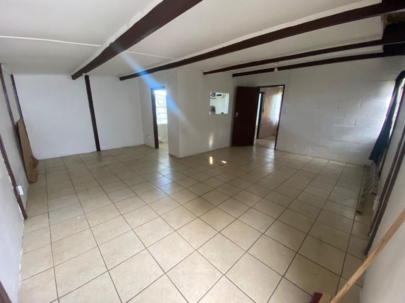An empty, open-plan living area featuring exposed ceiling beams, ceramic floor tiles, and a textured cinder block wall.