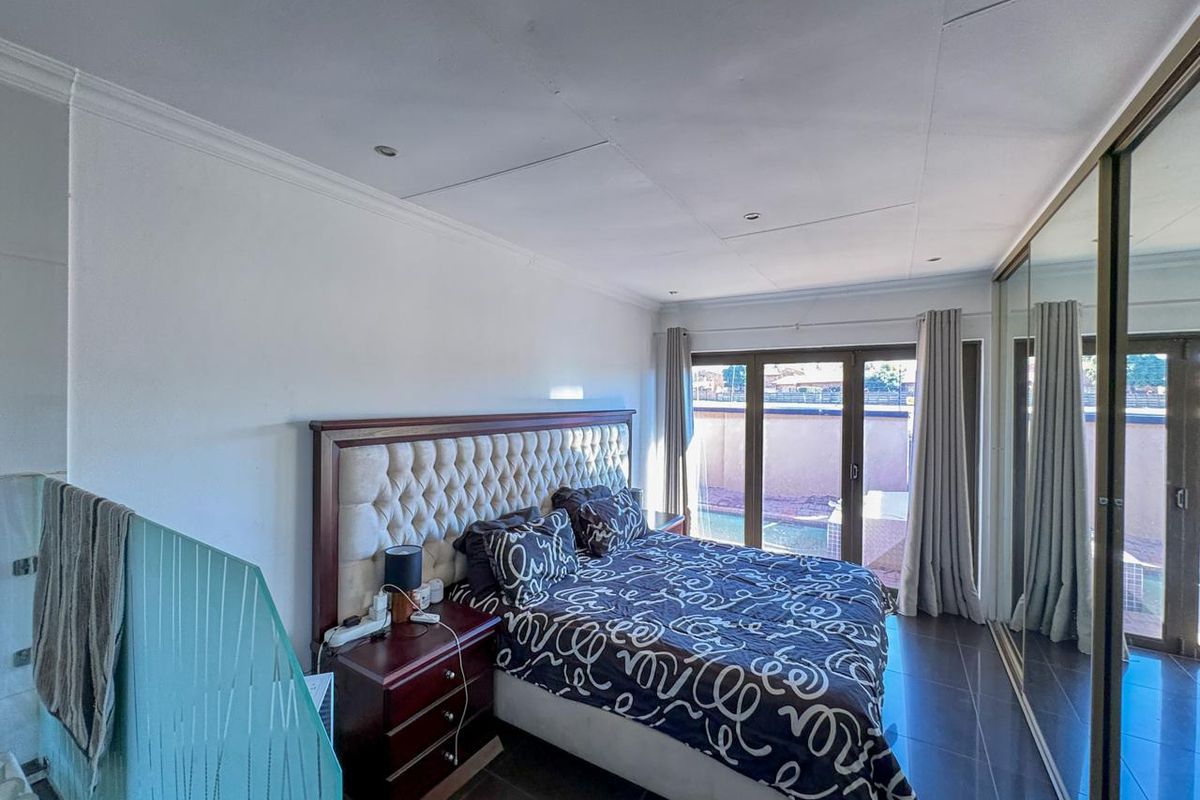 Spacious bedroom featuring tiled flooring, mirrored built-in cupboards, and sliding glass doors providing access to the outdoor area.