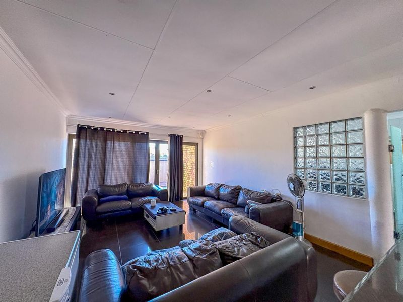 Spacious living room featuring dark tiled flooring, recessed downlighting, and a unique glass block feature wall, with direct access to an outdoor area.