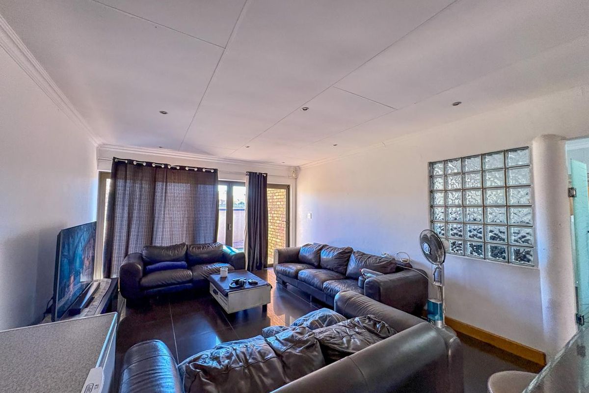 Spacious living room featuring dark tiled flooring, recessed downlighting, and a unique glass block feature wall, with direct access to an outdoor area.