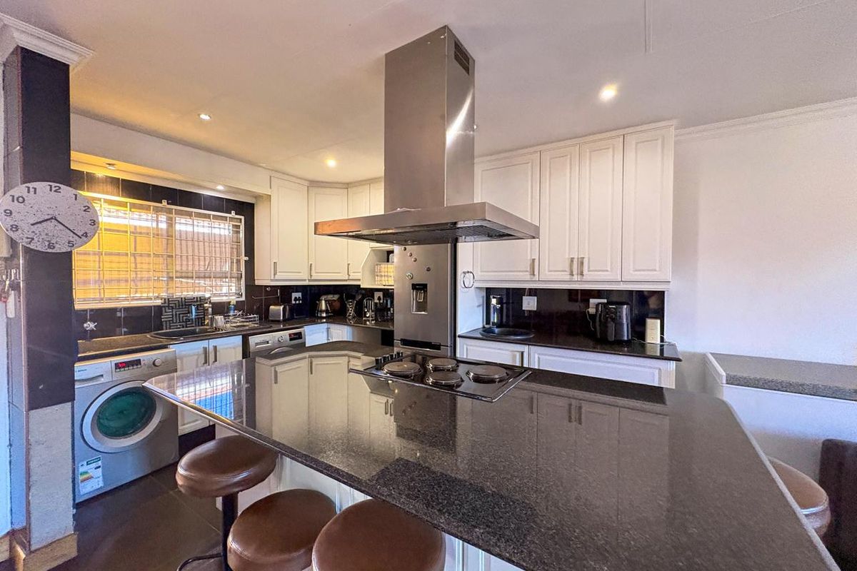A functional kitchen featuring granite countertops, a central island with a built-in hob, stainless steel extractor fan, and ample white cabinetry.
