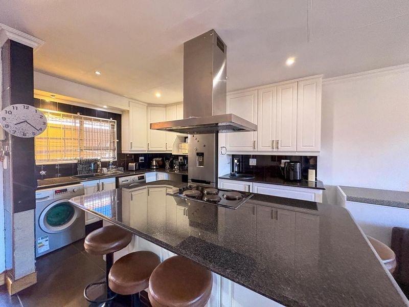 A functional kitchen featuring granite countertops, a central island with a built-in hob, stainless steel extractor fan, and ample white cabinetry.