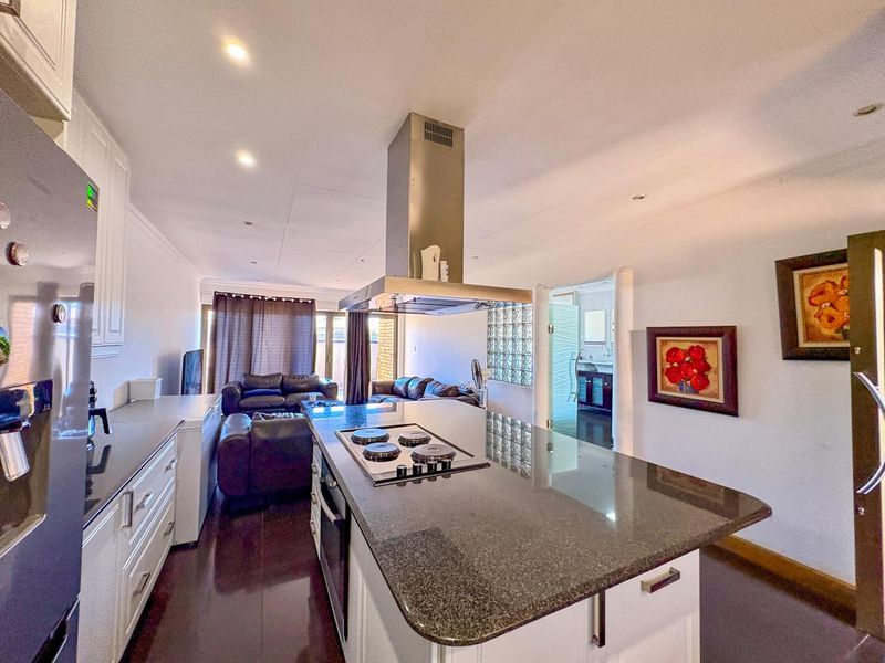 Open-plan kitchen and living area featuring a central island with granite countertops, built-in hob, extractor fan, and modern cabinetry.