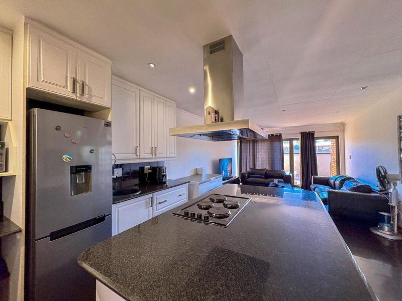 Open-plan living area featuring a modern kitchen with a central island, granite countertops, and a stainless steel extractor fan, flowing into the lounge space.