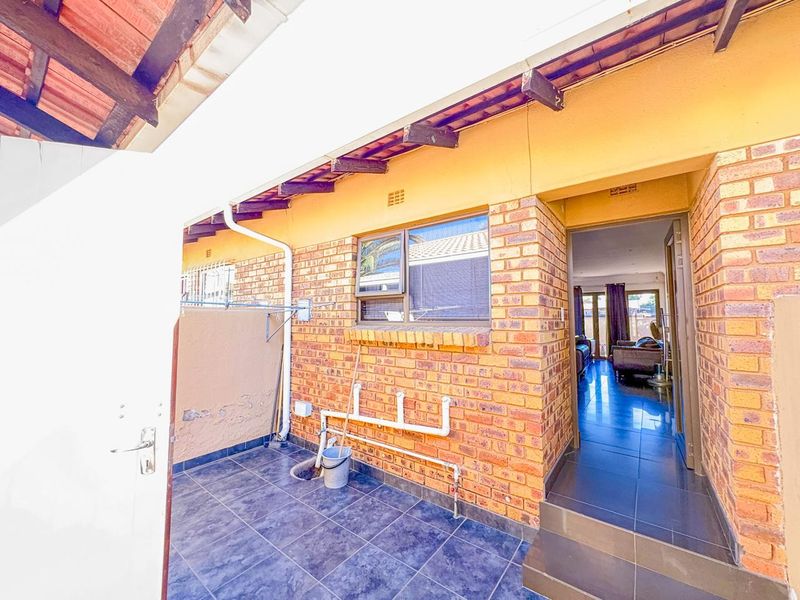 A covered outdoor patio area featuring facebrick walls, tiled flooring, and exposed timber rafters, providing direct access to the interior living space.