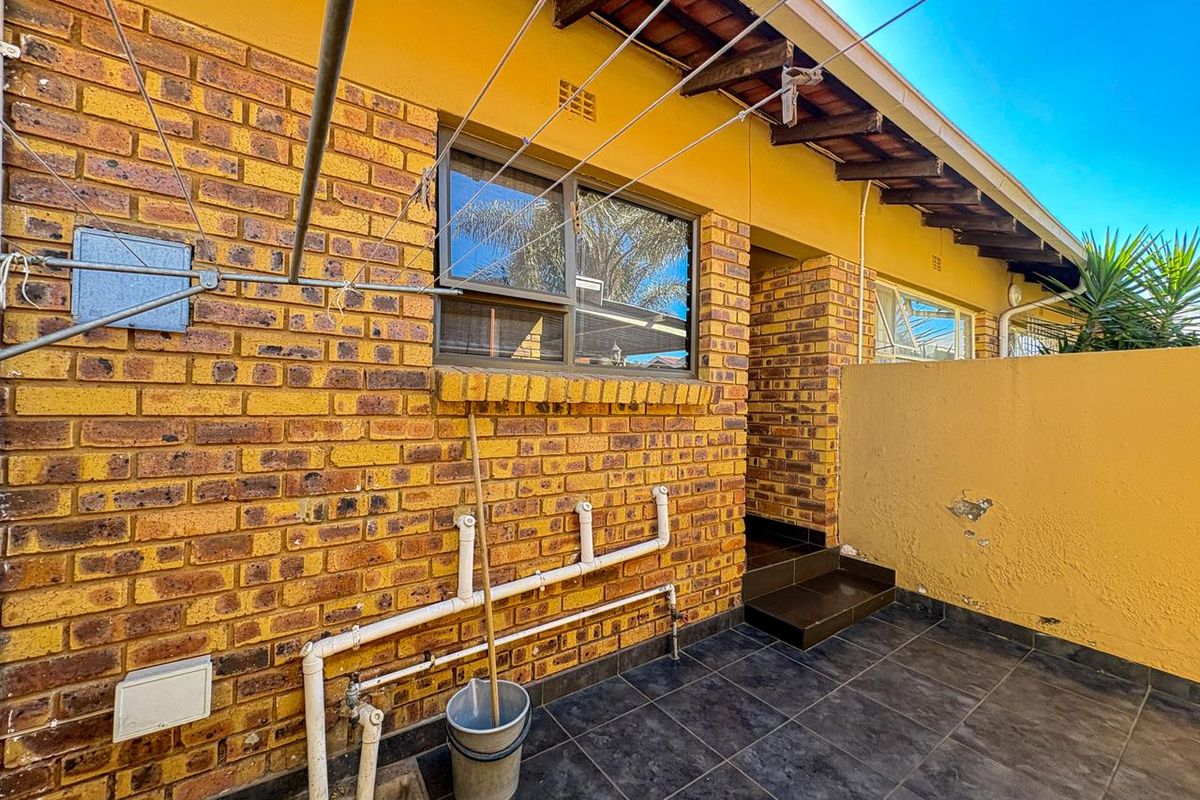 Rear exterior area featuring exposed brickwork, tiled patio flooring, external plumbing connections, and a wall-mounted washing line.