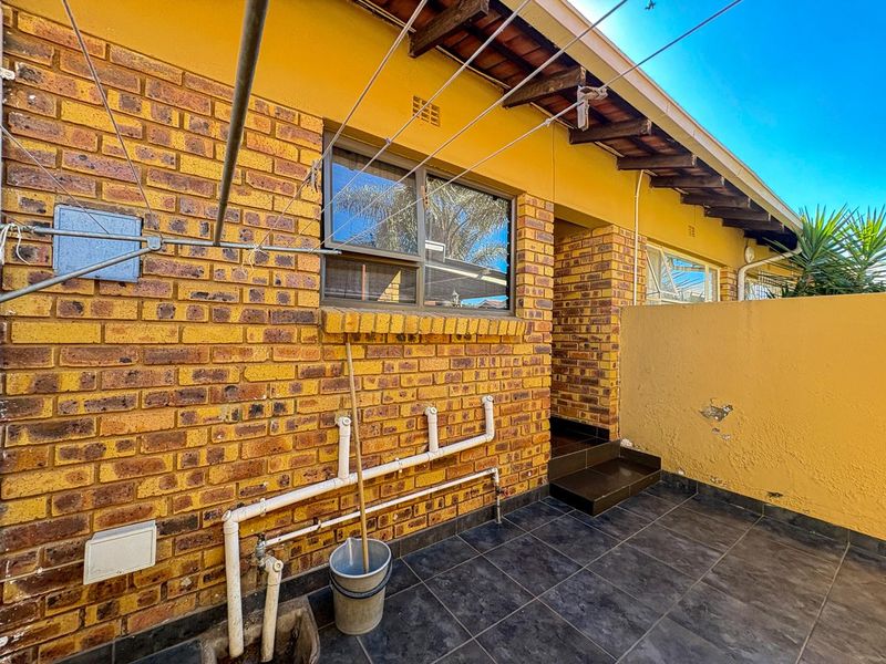 Rear exterior area featuring exposed brickwork, tiled patio flooring, external plumbing connections, and a wall-mounted washing line.