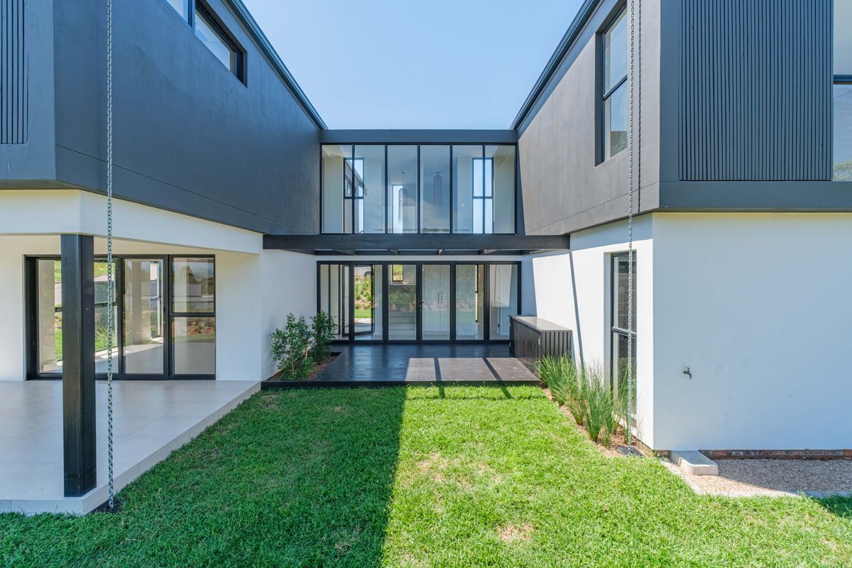 Modern rear courtyard featuring timber decking, expansive glass sliding doors, and a well-maintained lawn, creating a seamless indoor-outdoor living transition.