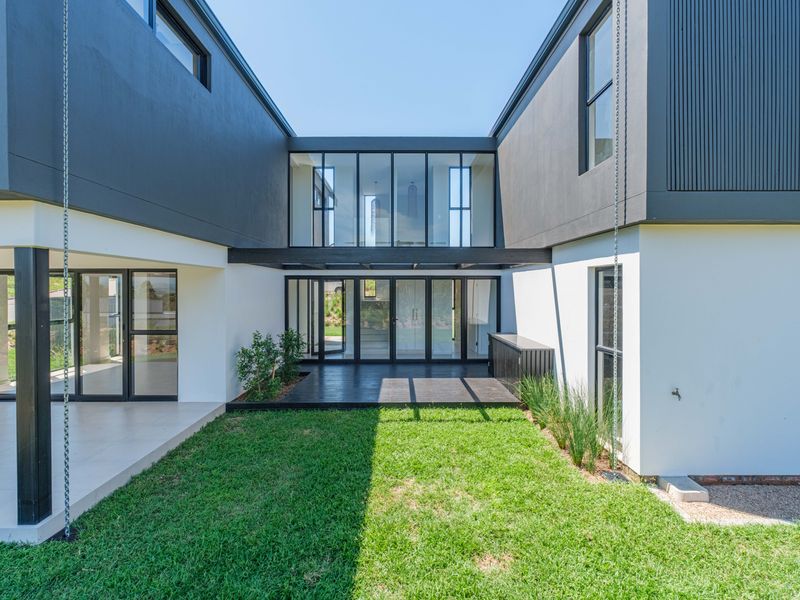 Modern rear courtyard featuring timber decking, expansive glass sliding doors, and a well-maintained lawn, creating a seamless indoor-outdoor living transition.