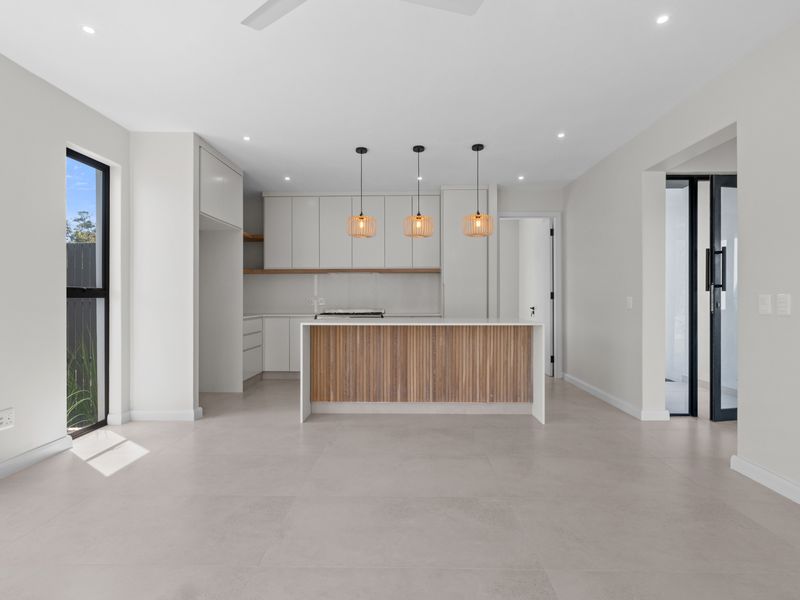 Modern open-plan kitchen featuring a central island with timber-look detailing, sleek cabinetry, and neutral tiled flooring in a bright, contemporary space.