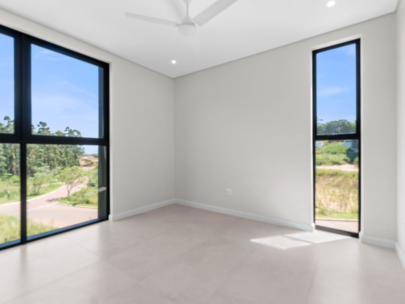 A bright, modern, and empty bedroom featuring large black-framed windows, tiled flooring, a ceiling fan, and recessed lighting with scenic exterior views.