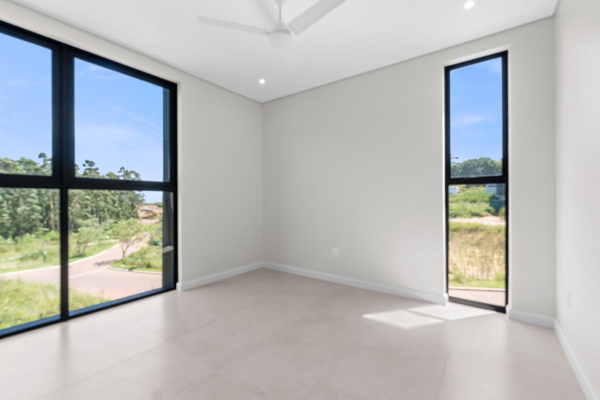 A bright, modern, and empty bedroom featuring large black-framed windows, tiled flooring, a ceiling fan, and recessed lighting with scenic exterior views.