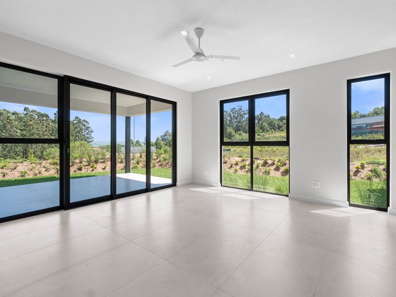 Bright and spacious living area featuring large black-framed windows, sliding glass doors to the patio, tiled flooring, and a modern ceiling fan.