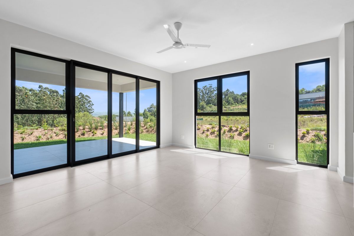 Bright and spacious living area featuring large black-framed windows, sliding glass doors to the patio, tiled flooring, and a modern ceiling fan.