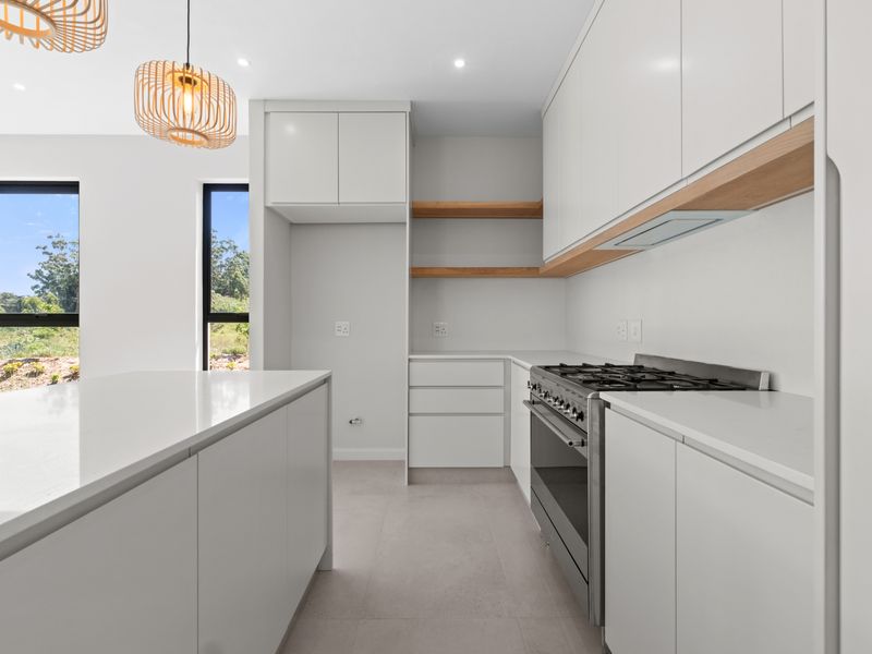 Modern kitchen featuring white cabinetry, quartz countertops, a central island, gas stove, and open shelving, finished with clean, contemporary lines.