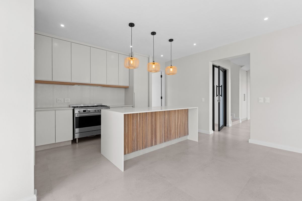 Modern kitchen featuring a central island with timber detailing, sleek white cabinetry, stone countertops, and a stainless steel gas stove.
