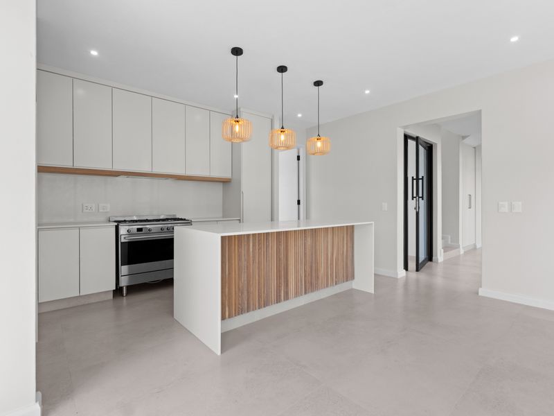 Modern kitchen featuring a central island with timber detailing, sleek white cabinetry, stone countertops, and a stainless steel gas stove.