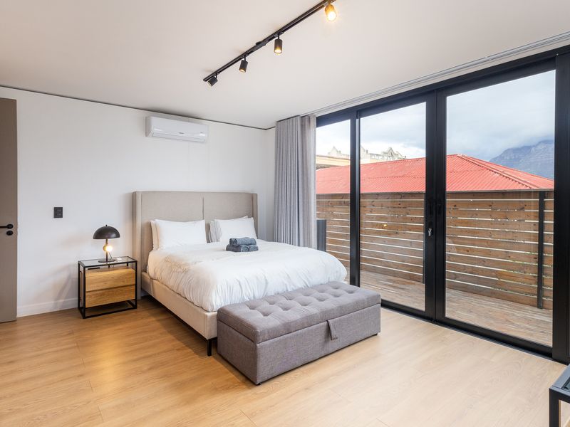 Modern bedroom featuring laminate flooring, track lighting, a wall-mounted air conditioner, and large sliding glass doors providing access to an outdoor deck area.