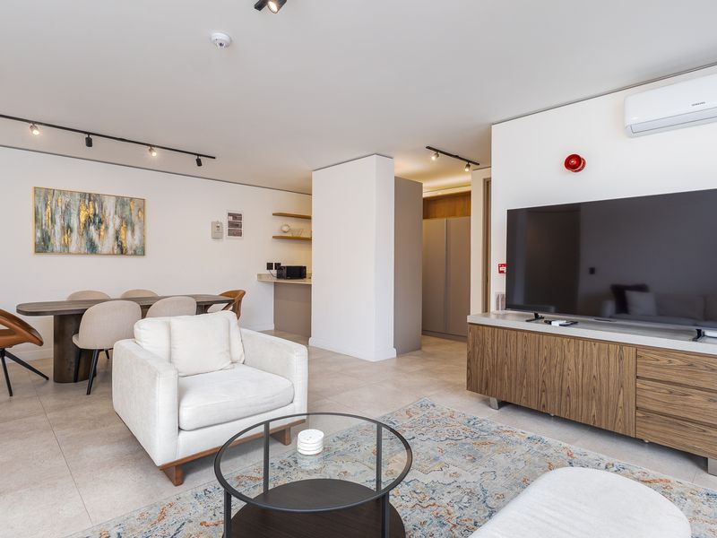 Modern open-plan living and dining area featuring neutral tiled flooring, contemporary track lighting, and integrated air conditioning in a well-maintained apartment setting.