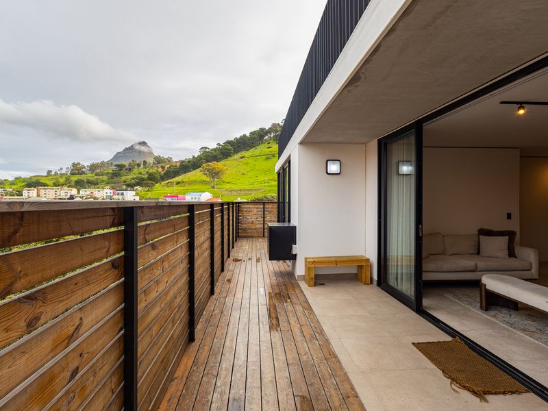 Spacious balcony featuring timber decking and a wooden balustrade, offering scenic mountain views and seamless access to the interior living area through sliding doors.