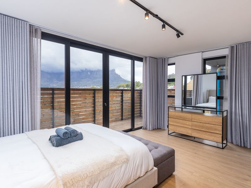 Modern bedroom featuring laminate flooring, track lighting, and large sliding glass doors opening onto a private balcony with mountain views.