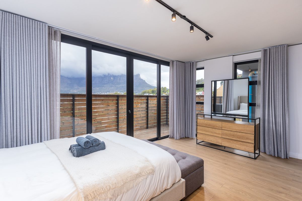 Modern bedroom featuring laminate flooring, track lighting, and large sliding glass doors opening onto a private balcony with mountain views.