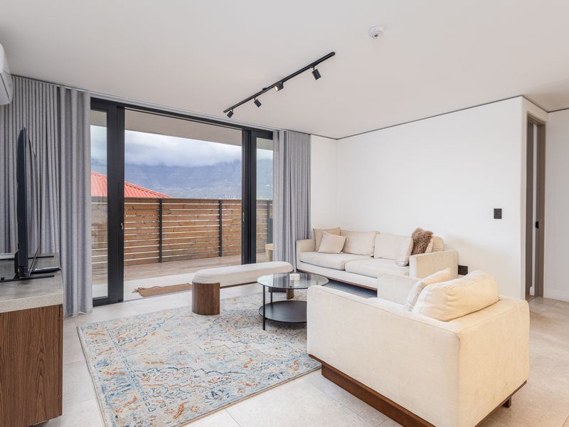 Modern living room featuring tiled floors, track lighting, and large sliding glass doors that open onto a private balcony with mountain views.