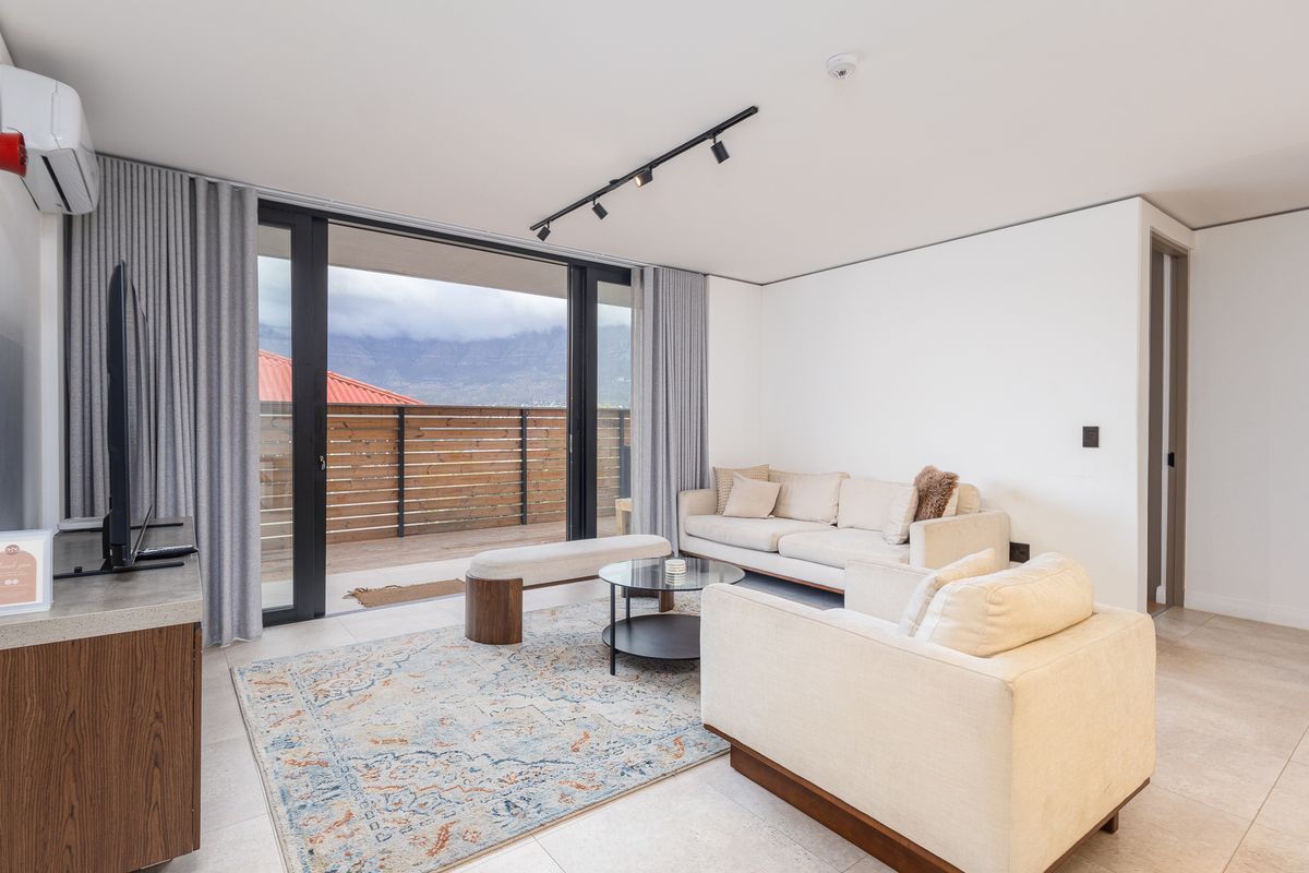 Modern living room featuring tiled floors, track lighting, and large sliding glass doors that open onto a private balcony with mountain views.