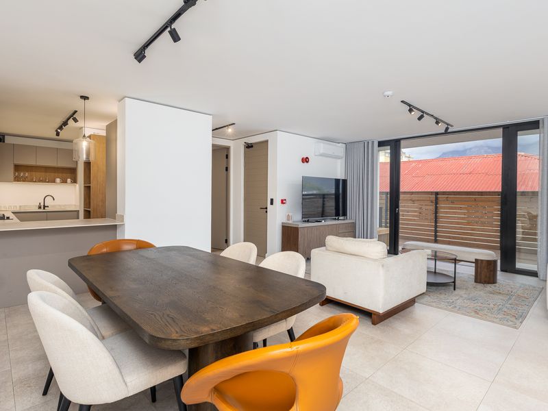 Modern open-plan living and dining area featuring sleek kitchen cabinetry, track lighting, and seamless access to a private balcony through large sliding glass doors.