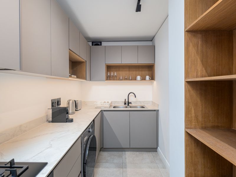 Modern scullery featuring sleek grey cabinetry, stone countertops, integrated washing machine, double sink, and warm under-cabinet lighting.