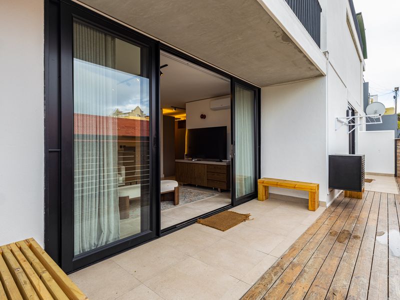 A modern balcony featuring a combination of tiled flooring and timber decking, accessible through large black-framed sliding glass doors.