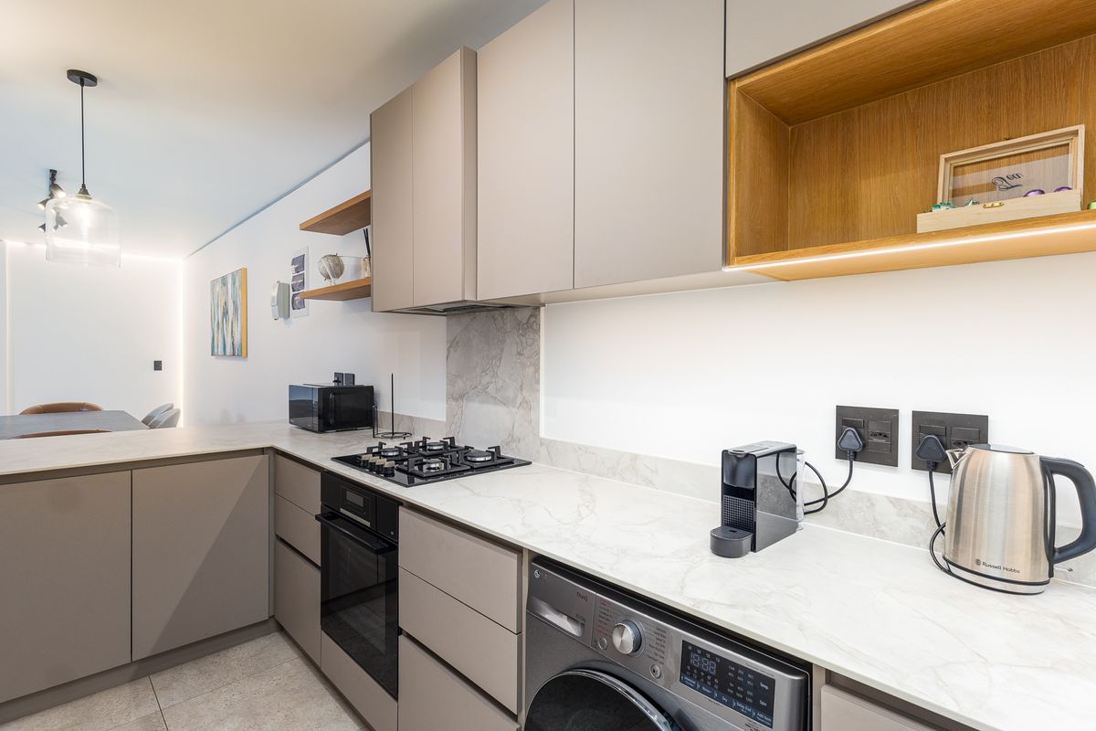 Modern kitchen featuring sleek handleless cabinetry, stone countertops, integrated appliances, and a gas hob with a stylish stone splashback.