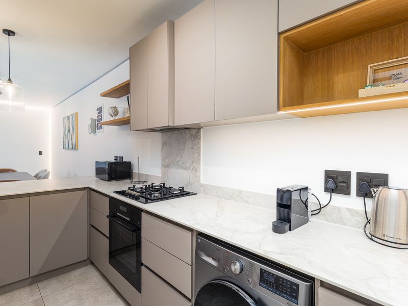 Modern kitchen featuring sleek handleless cabinetry, stone countertops, integrated appliances, and a gas hob with a stylish stone splashback.