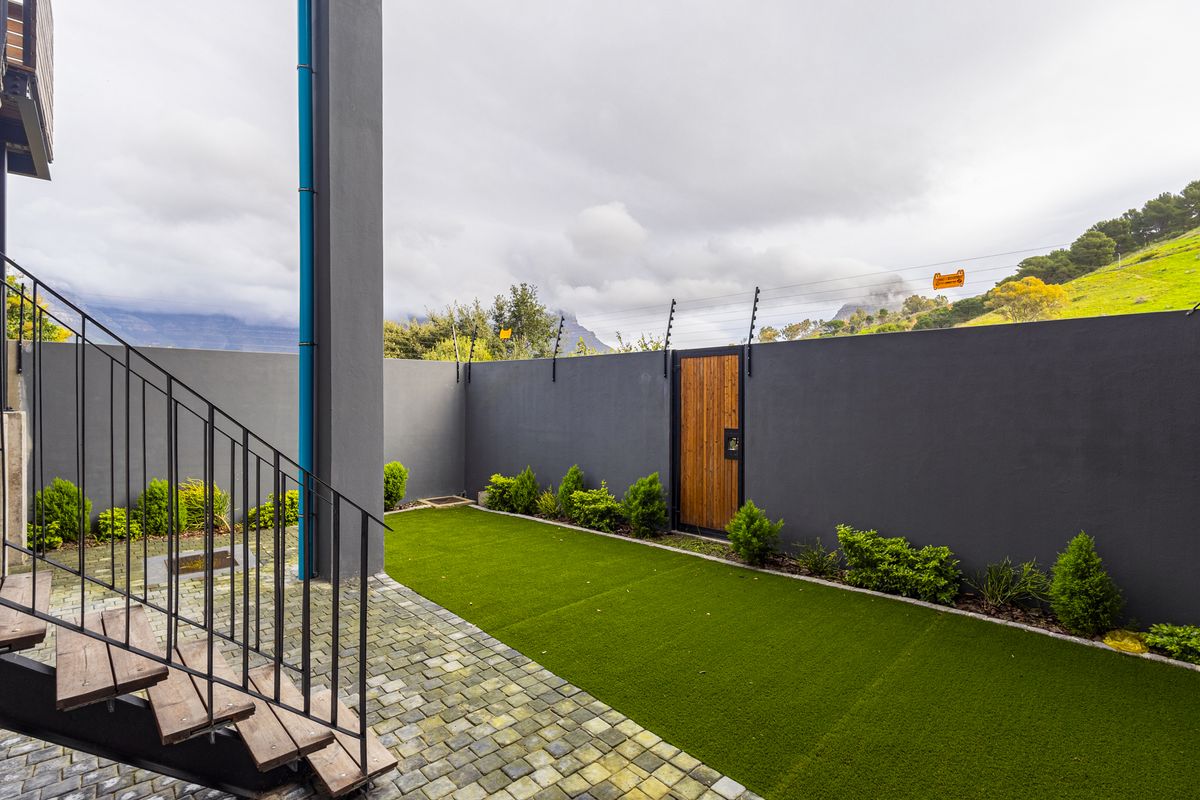 A private rear courtyard featuring a paved patio, artificial lawn, secure boundary wall with electric fencing, and a timber pedestrian gate.