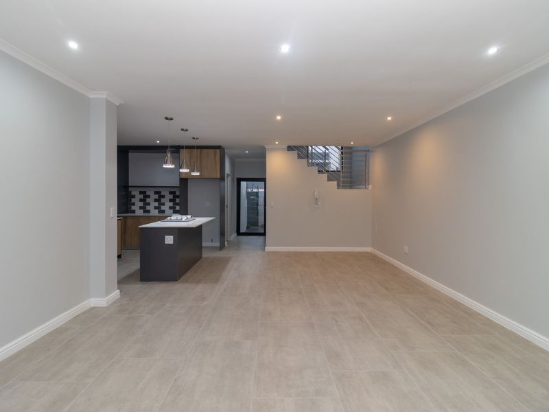 Spacious open-plan living area featuring modern tiled flooring, recessed lighting, and a contemporary kitchen with a central island and staircase.