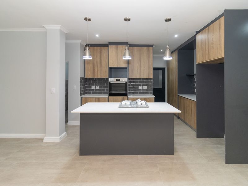 Modern kitchen featuring a central island, built-in oven, stone countertops, and contemporary two-tone cabinetry with a stylish subway tile backsplash.