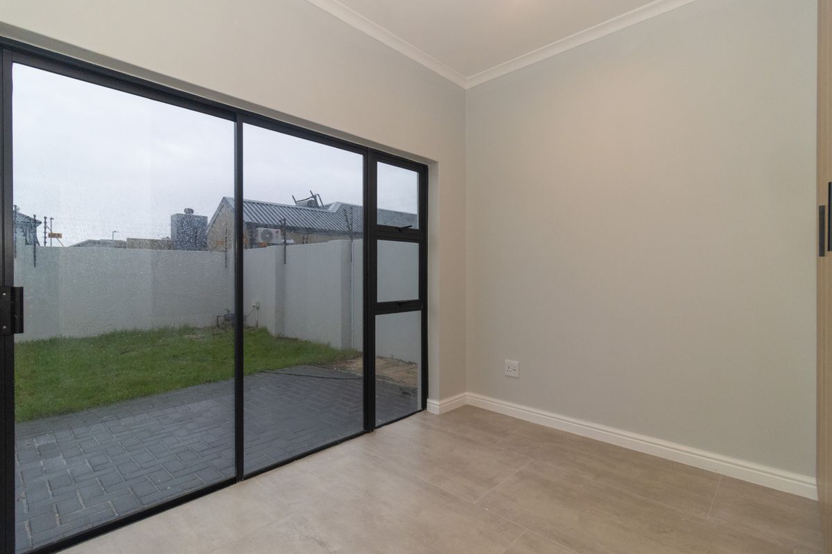 A bright, empty bedroom featuring modern tiled flooring and a large sliding glass door providing direct access to the rear garden area.