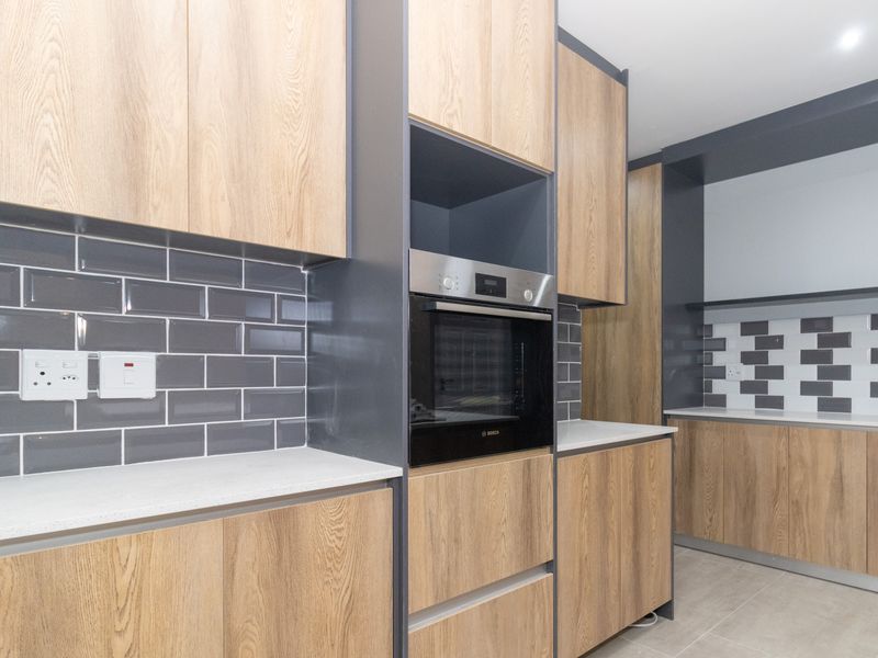 Modern kitchen featuring light wood cabinetry, dark grey subway tile backsplash, stone countertops, and a built-in oven.