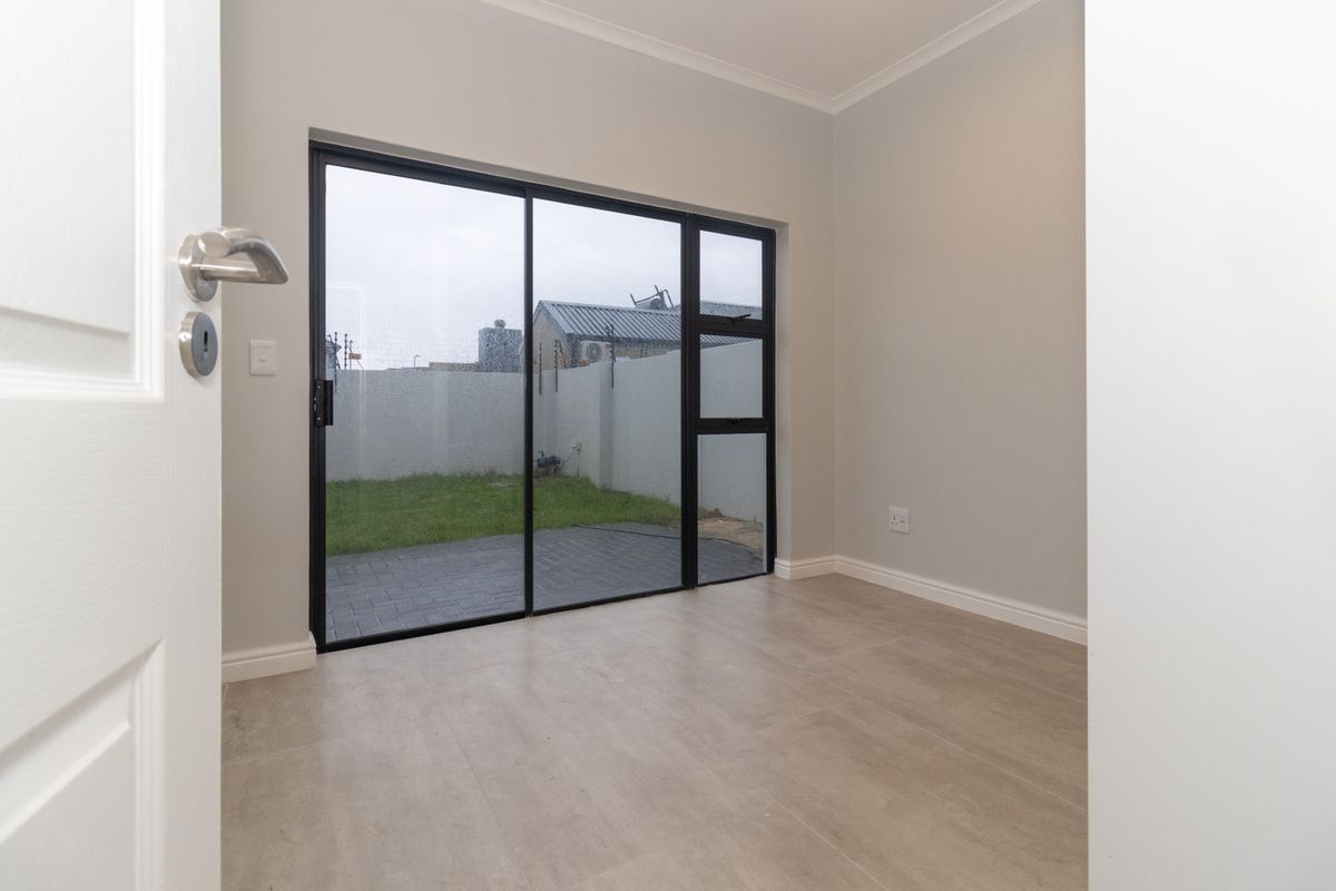 A bright, empty living room featuring modern tiled flooring and a large sliding glass door providing direct access to the rear garden.