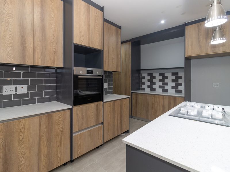 Modern kitchen featuring wood-tone cabinetry, stone countertops, subway tile backsplash, built-in oven, and a central island with integrated cooktop.