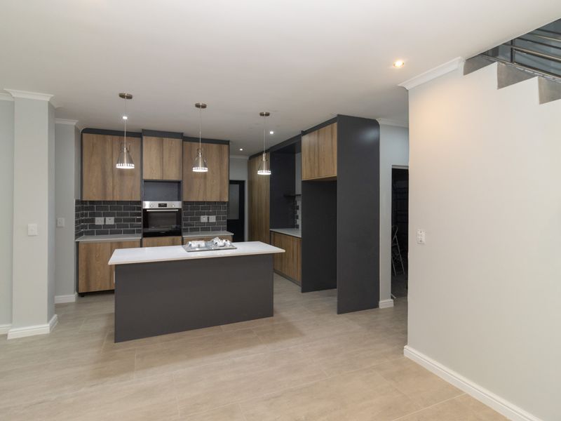 Modern kitchen featuring two-tone cabinetry, a central island with stone countertops, built-in oven, and stylish subway tile backsplash, adjacent to a staircase.