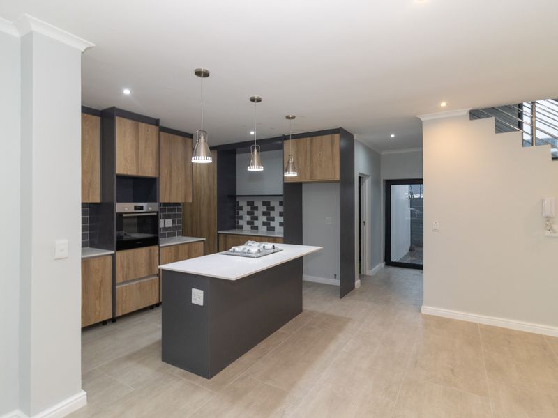 Modern kitchen featuring a central island, built-in oven, hob, and contemporary cabinetry, seamlessly integrated into an open-plan living space with staircase access.