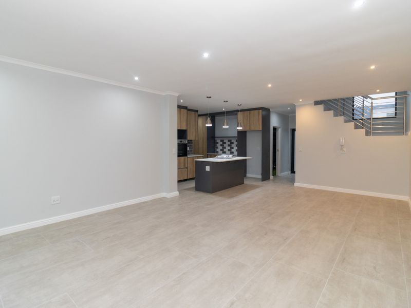 Spacious open-plan living area featuring a modern kitchen with a central island, tiled flooring, and a staircase with a contemporary metal balustrade.