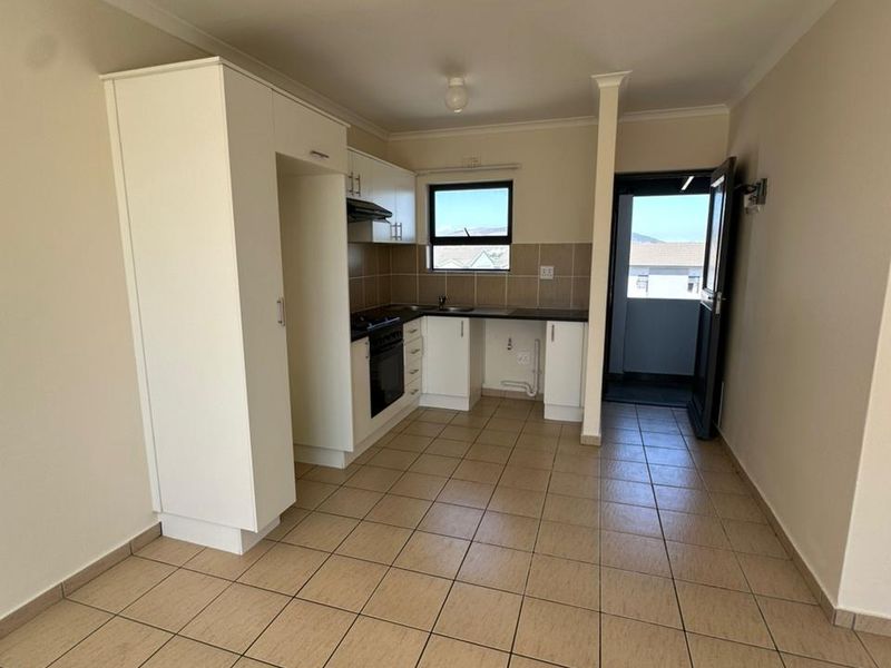 A functional, empty kitchen featuring tiled flooring, built-in cabinetry, and integrated appliances, with direct access to an outdoor balcony area.