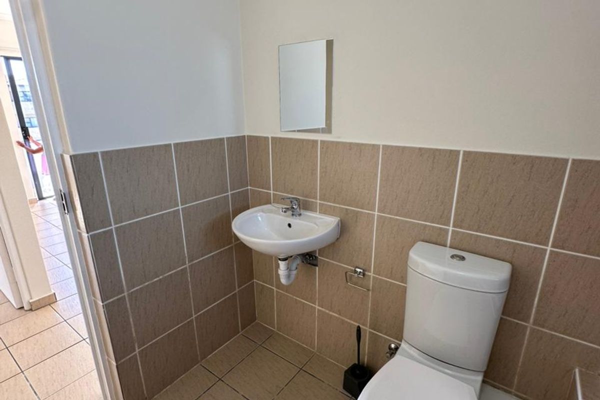 A functional guest bathroom featuring a wall-mounted basin, toilet, and neutral ceramic tiling throughout.