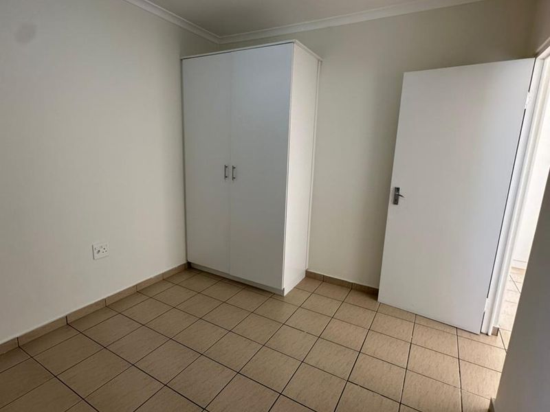 A clean, empty bedroom featuring neutral tiled flooring, a built-in wardrobe, and simple finishes, ready for personalization.