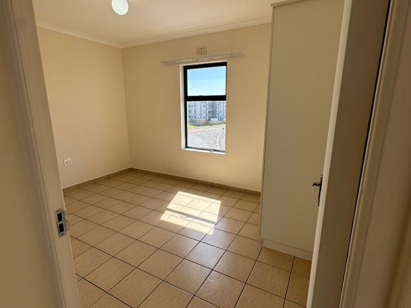 A clean, empty bedroom featuring neutral tiled flooring, a built-in wardrobe, and a window providing natural light.
